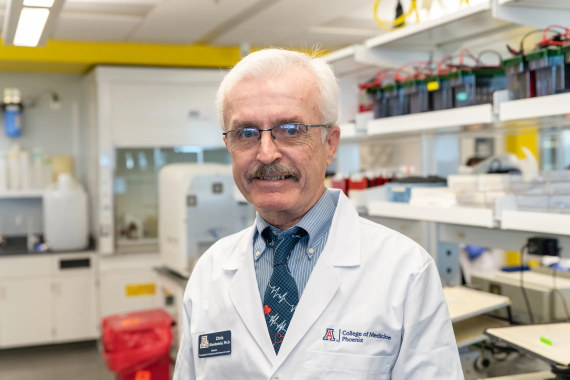 A person wearing a lab coat with a "College of Medicine, Phoenix" badge standing in a laboratory setting