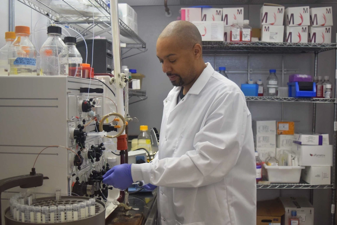 A scientist wearing a lab coat and gloves is working with samples in a centrifuge in a well-equipped laboratory.