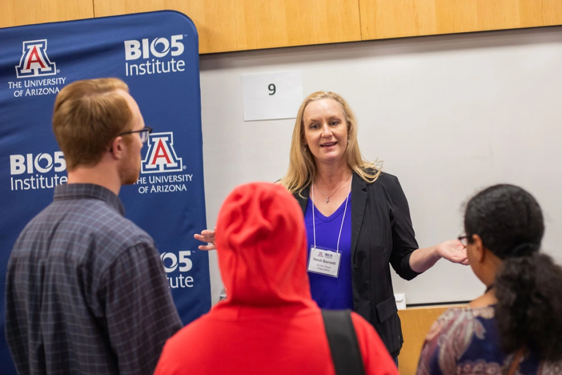 Person presenting at a University of Arizona BIO5 Institute event, interacting with three attendees in front of informational banners.
