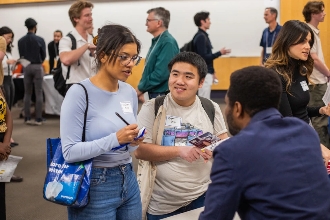 Group of people engaging in conversation at a networking event, some holding brochures and wearing name tags.