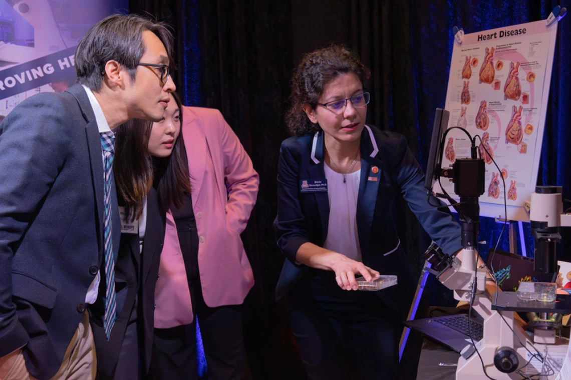 Three professionals are examining a scientific display about heart disease at an event, featuring informational posters and lab equipment.