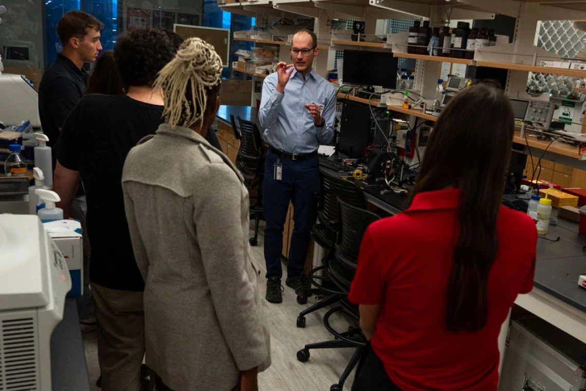 A group of people listening to a scientist in a laboratory filled with equipment.