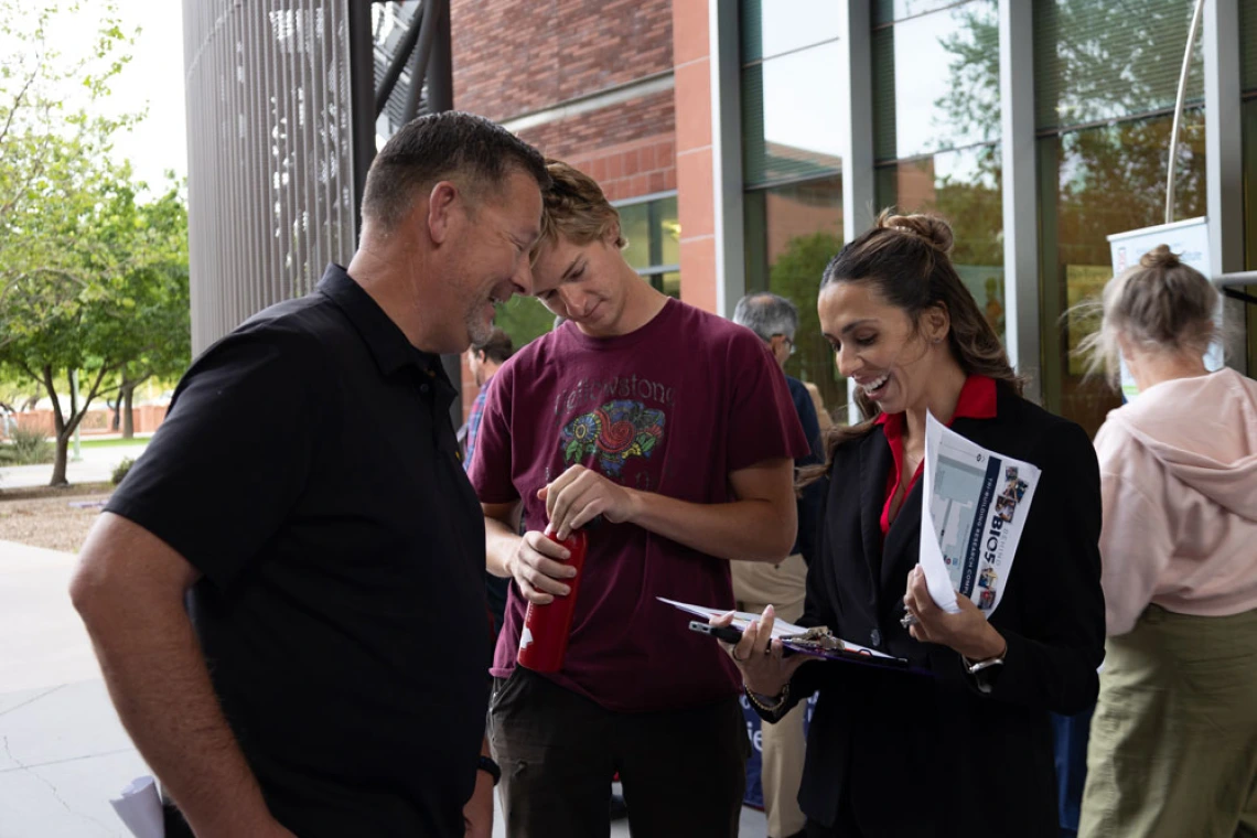Three individuals engaged in a friendly interaction outside a building, with one person showing at something on a clipboard to the others.