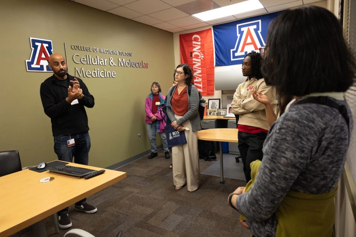 Group of adults engaging in a discussion in a University of Arizona classroom, with banners reading "College of Medicine - Tucson" and "Cellular & Molecular Medicine" in the background.