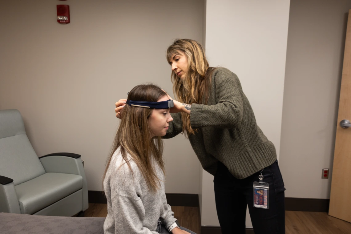 A healthcare professional is using a headband to measure a patient's head in a medical office.