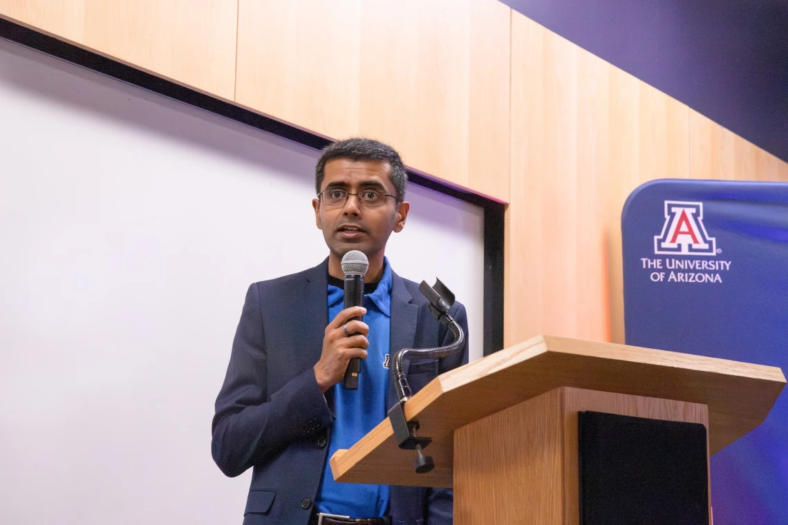 Person speaking at a podium with a microphone at a University of Arizona event.
