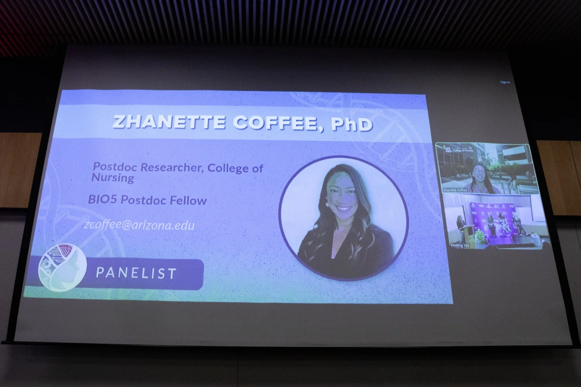 Presentation slide on a large screen showing "Zhanette Coffee, PhD, a Postdoc Researcher at the College of Nursing, BIO5 Postdoc Fellow, with contact email. The slide includes a portrait and designates them as a panelist.