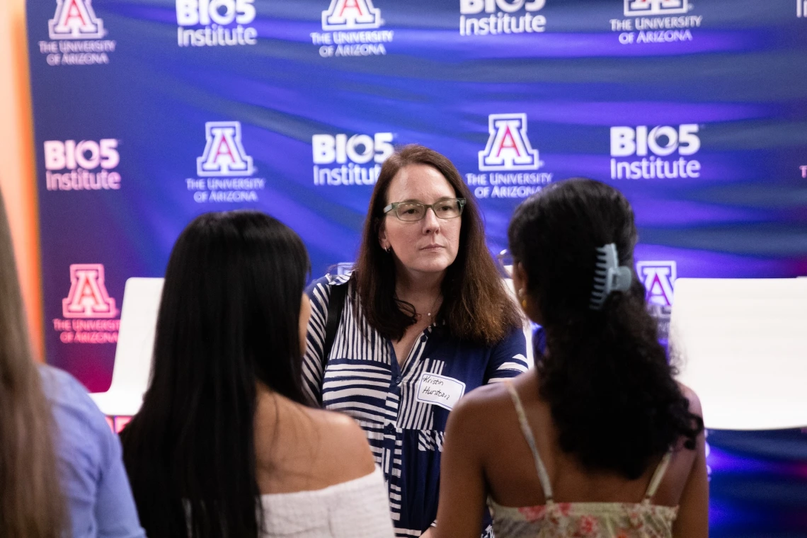 Person wearing a name tag converses with two others at an event hosted by the BIO5 Institute at the University of Arizona.