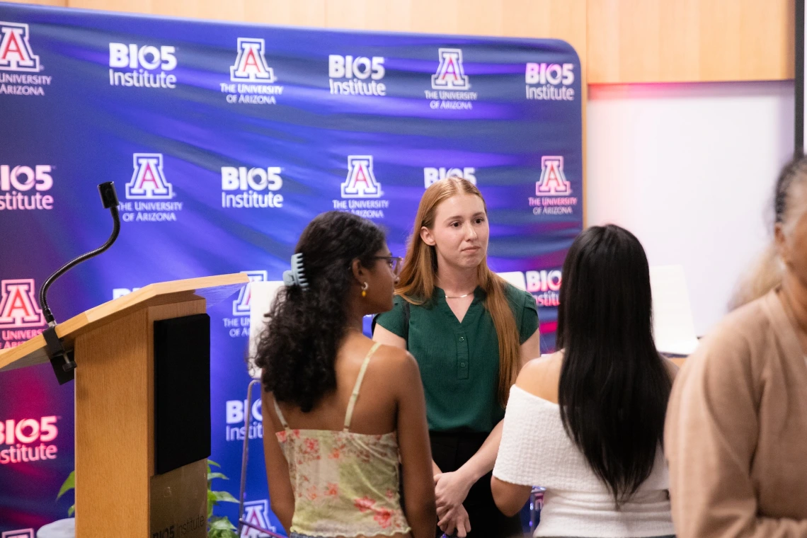 Three people conversing in front of a backdrop with the University of Arizona and BIO5 Institute logos.