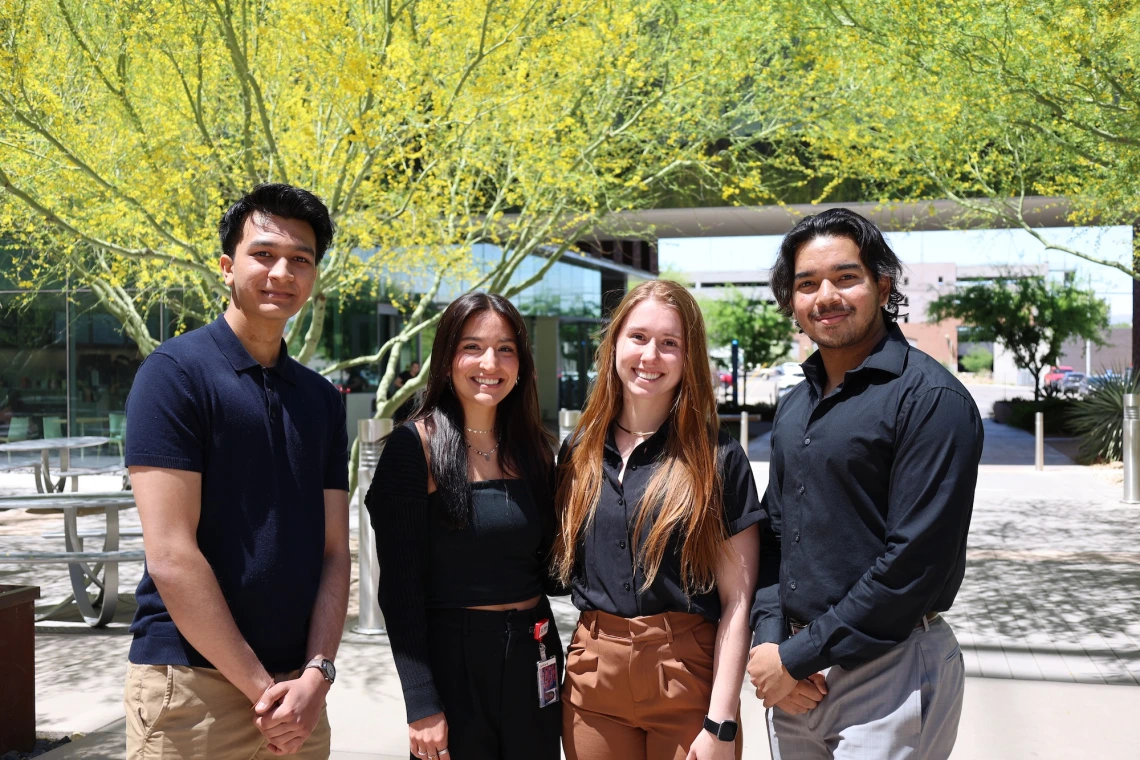 Four people smiling for the camera in a sunny outdoor setting with vibrant yellow trees in the background.