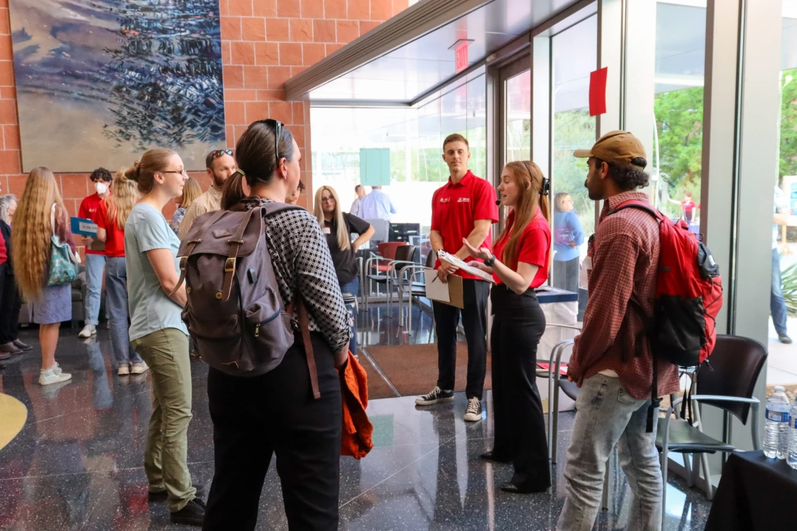 Students and staff in red shirts handing out materials during a university event in a lobby.