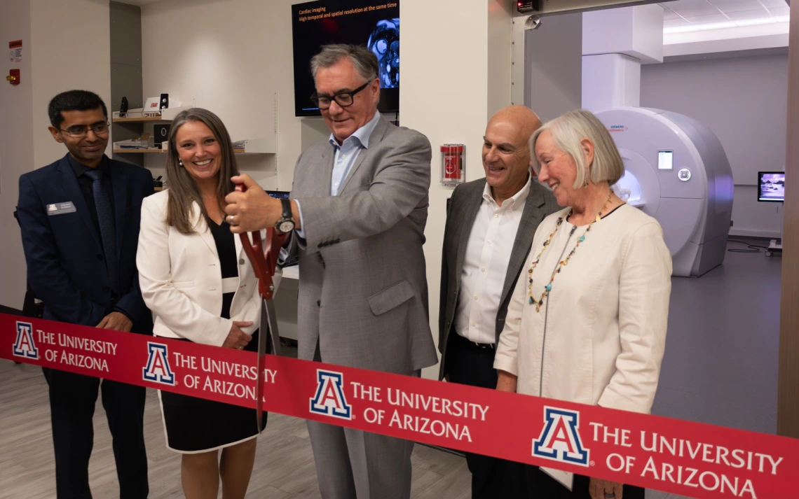 Group of five individuals participating in a ribbon-cutting ceremony at the University of Arizona, with a medical imaging machine in the background.