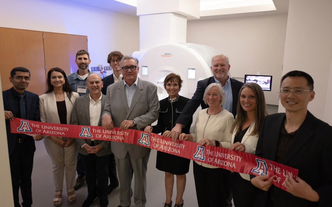 Group of individuals holding University of Arizona banners in front of an MRI machine.