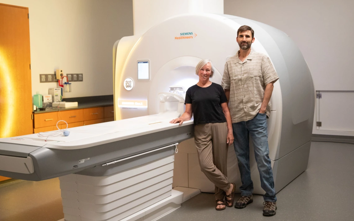 Two individuals standing next to a Siemens MRI machine in a research facility.