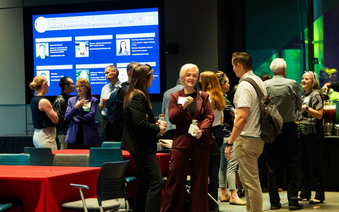Group of people networking at a faculty insight evening event, with a digital display in the background featuring information about participants.