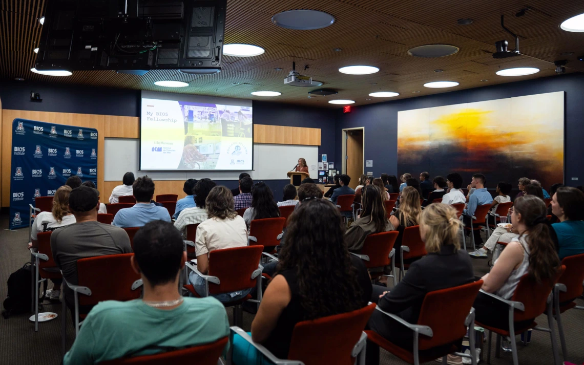 A person delivers a presentation on their fellowship at the BIO5 Institute, audience listens attentively in a modern lecture hall.