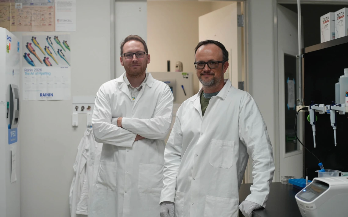 Two people in lab coats are standing in a laboratory.