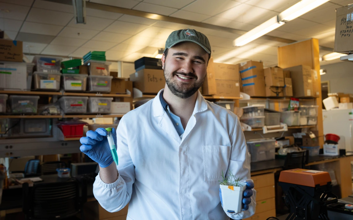 Man in lab gear holding a plant and green vial