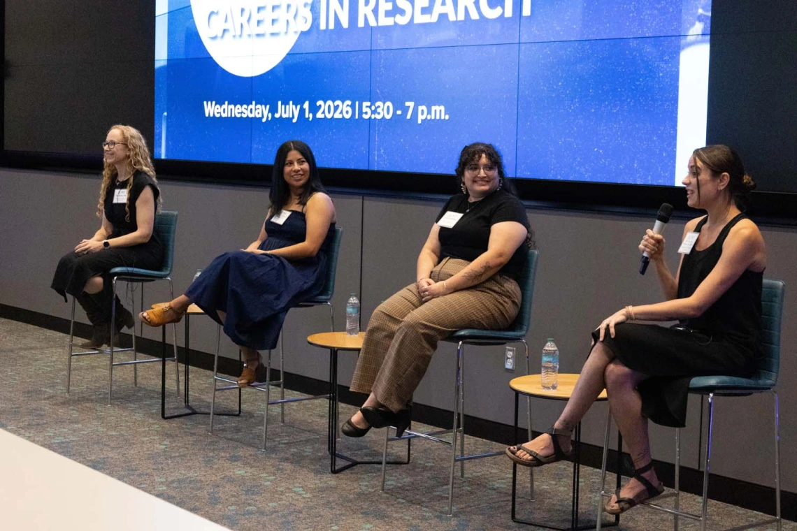 A panel discussion featuring four individuals seated in front of a large screen displaying the text "Careers in Research"