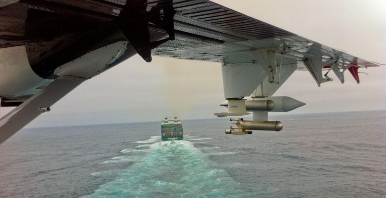 A plane wing above a shipping vessel in the ocean