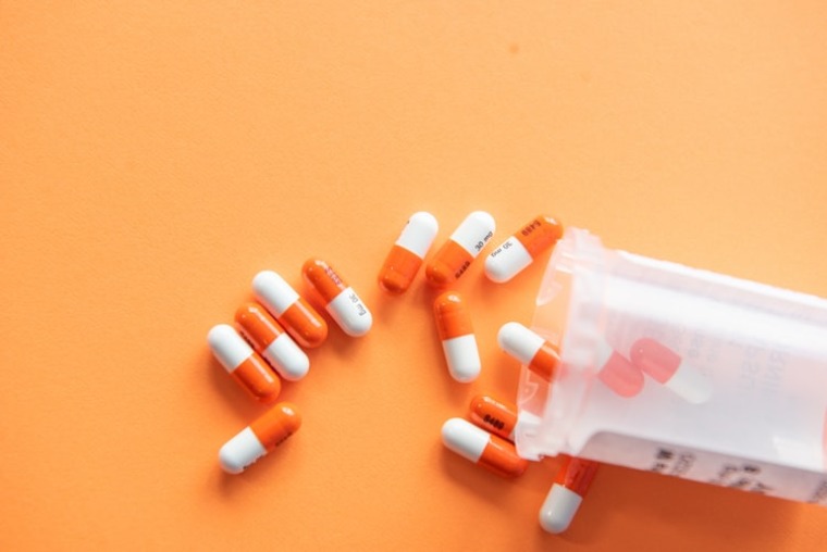 Orange and white pills spilling out of a pill bottle on an orange table. Christina Craft, Unsplash