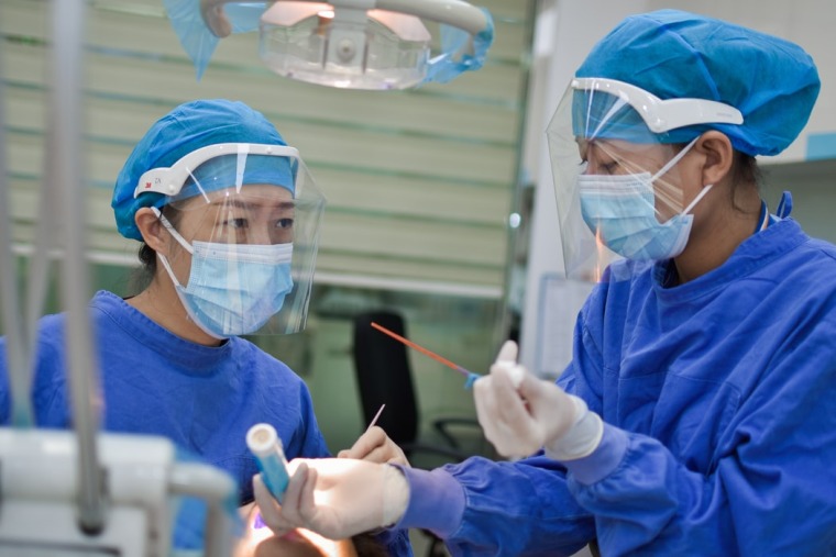 Two female doctors wearing blue scrubs, bonnets and masks during a surgery - H Shaw, Unsplash