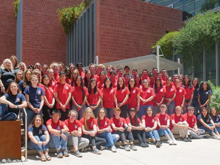 Group photo of high school students in red and blue shirts, sitting and standing outside a building