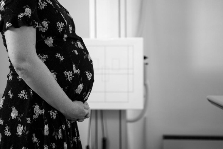 Black and white photo of pregnant woman wearing a flowered dress, holding her belly 