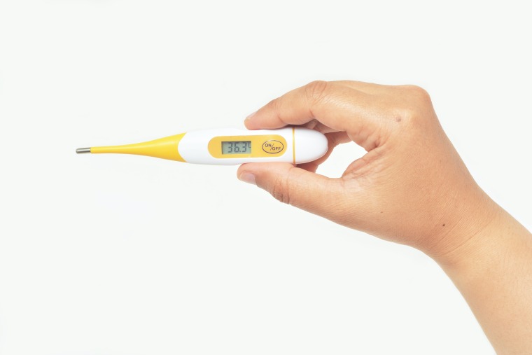 Right hand holding a yellow and white digital thermometer which reads 36.6 celsius