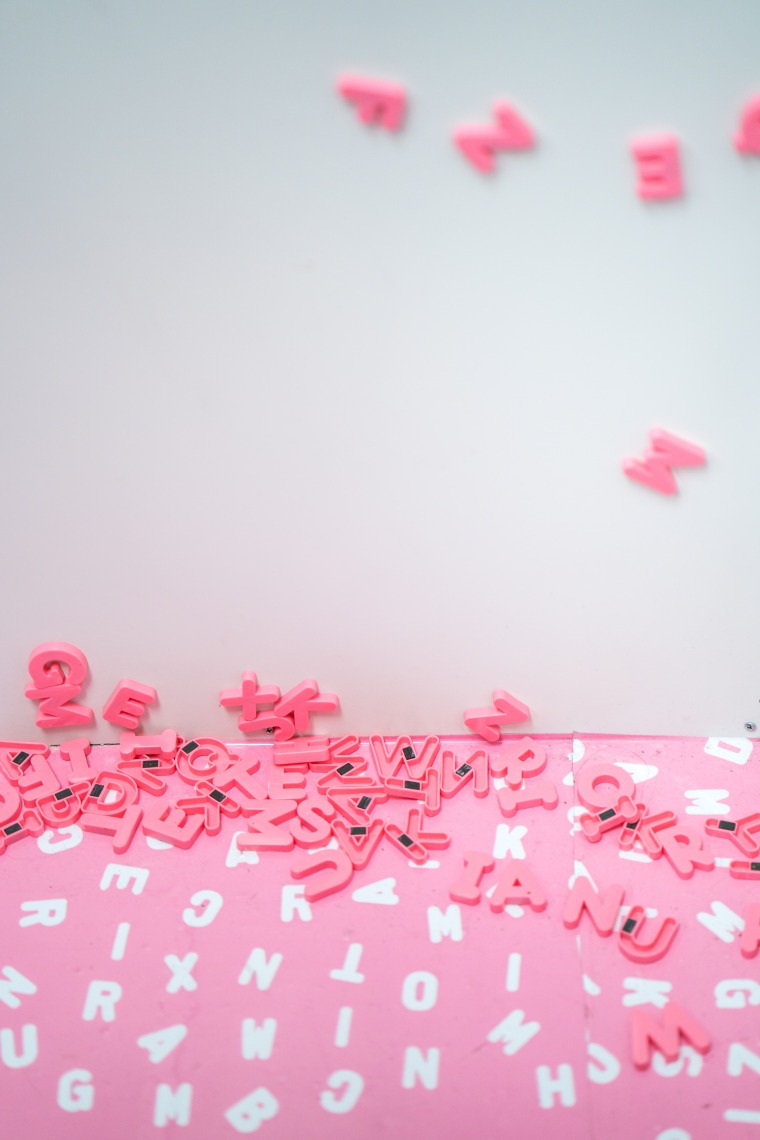 Pink magnetic letter scattered on a while wall and across a pink surface with white letters