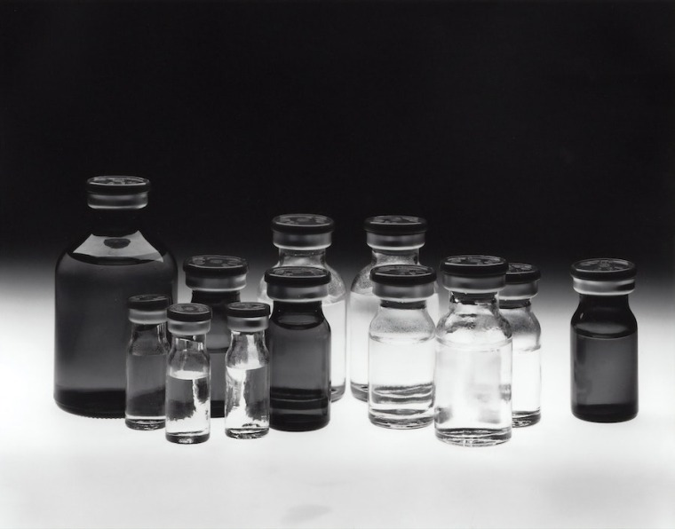 Gray and clear glass vials of liquid on a lit surface