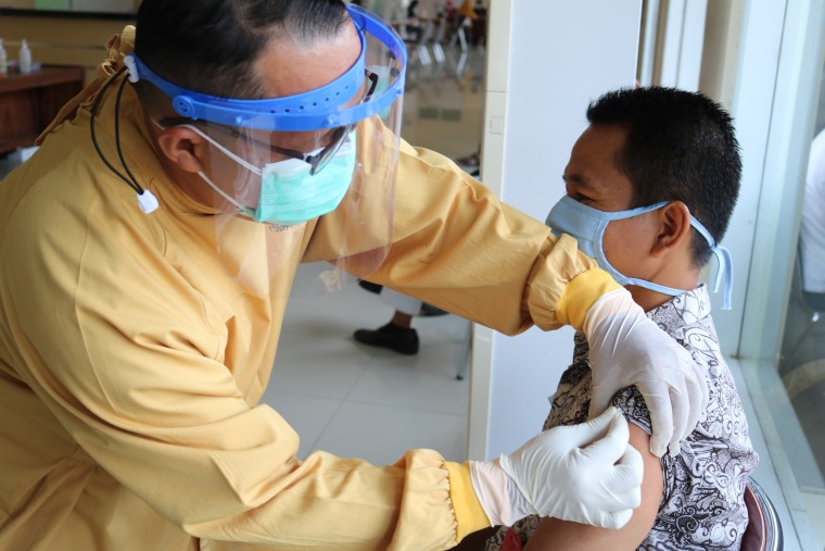 A Doctor in a yellow hazmat suit and face shield finishing up a vaccination of another man 