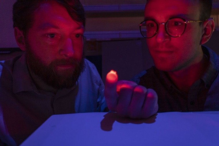 Dr. Philipp Gutruf and Jokubas Ausra dimly lit with a glowing, red optogenetics device
