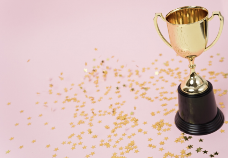 A trophy with star sparkles laying around set on a pink background