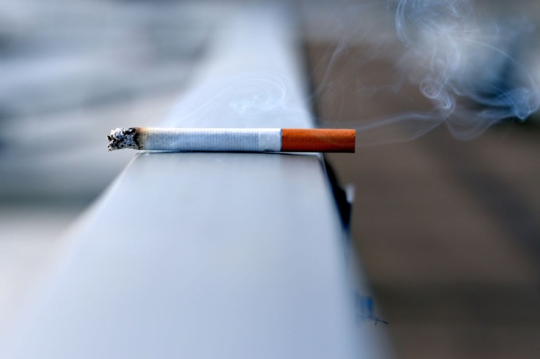 A burning cigarette sits on a hand rail