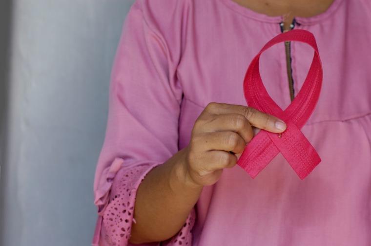 Person in pink shirt holds pink bow to symbolize breast cancer