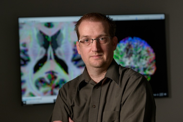 Adam Raikes in front of colorful brain images.