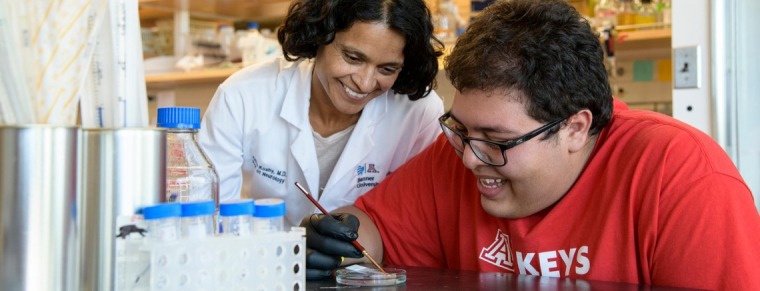Dr. Anita Koshy wearing a white lab coat, smiling with boy student intern wearing a red tshirt