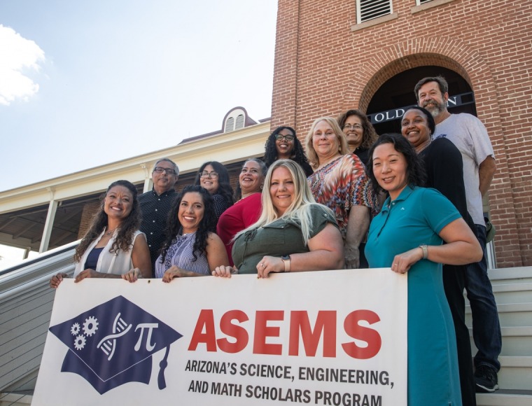 UArizona faculty pose and smile in front of old main carrying an ASEMS sign