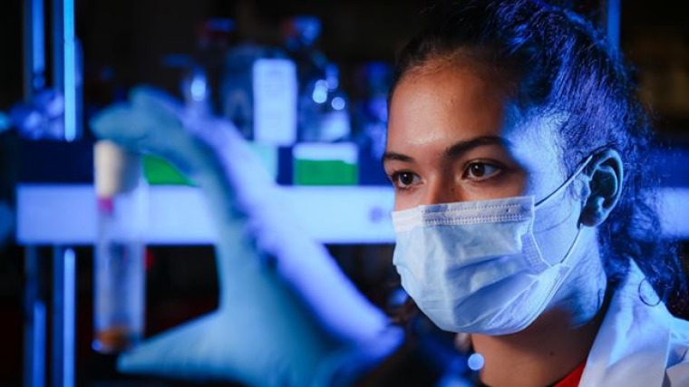 Grace Hala’ufia looking at sample in a lab with blue lighting.