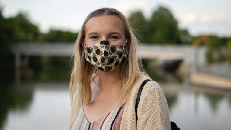 Woman in a mask in front of a lake.