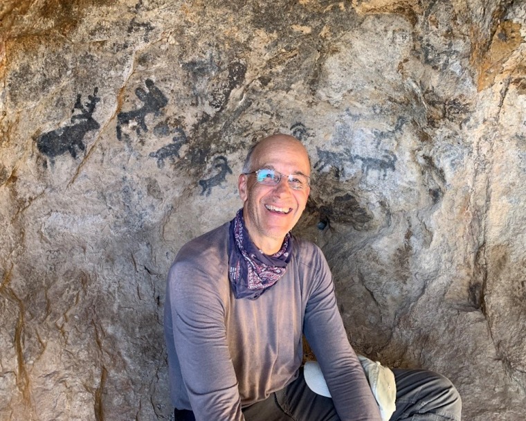 Bernard Futscher smiling int front of rock with ancient paintings on it.