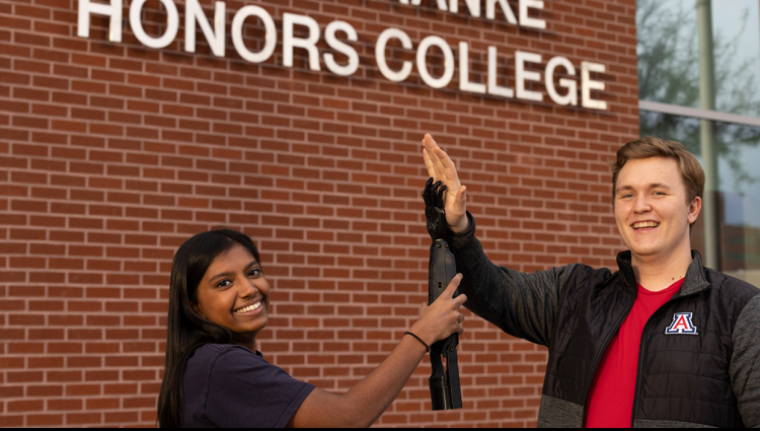 Two Biomedical Engineering Students holding up a prosthetic arm in a high-five motion.