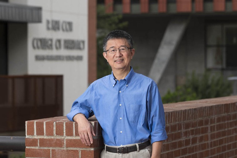 Dr. Xinxin Ding leaning on a brick wall.