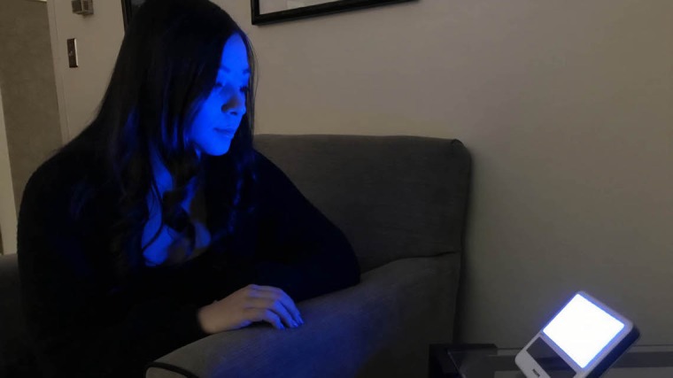 A woman sitting next to a device with blue light being emitted. 