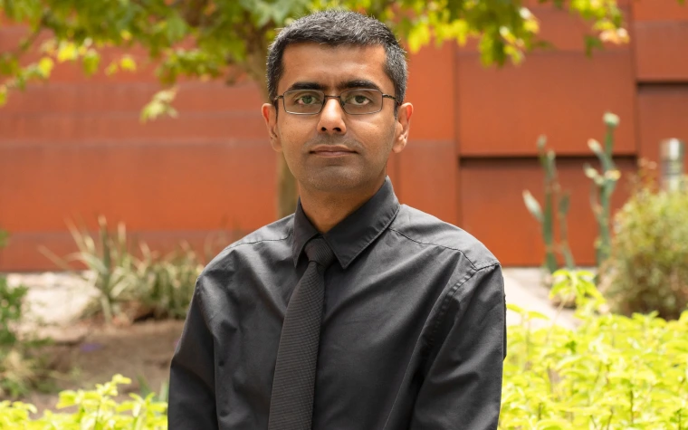 Person in a black shirt standing in front of a red brick wall with greenery around.