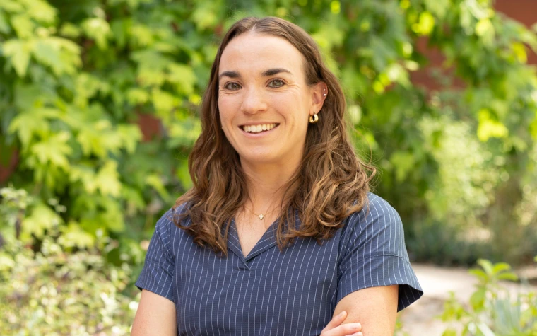 Person in a blue shirt smiling against a backdrop of greenery