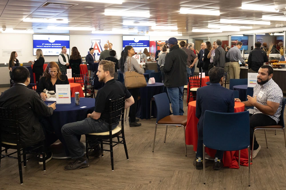 Attendees networking at a University of Arizona event in a conference room with tables, chairs, and promotional banners.