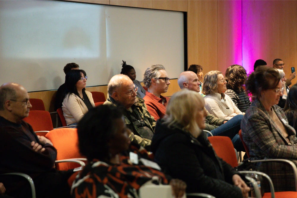 Audience members sitting attentively in a conference room with ambient lighting.