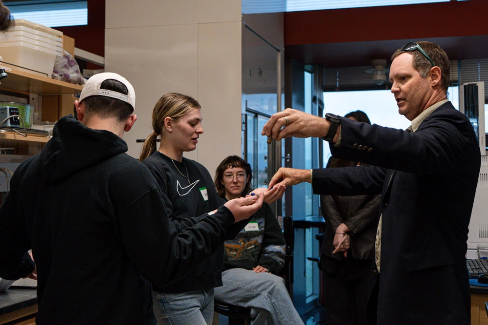 A group of students participates in a hands-on demonstration led by an scientist in a laboratory setting.